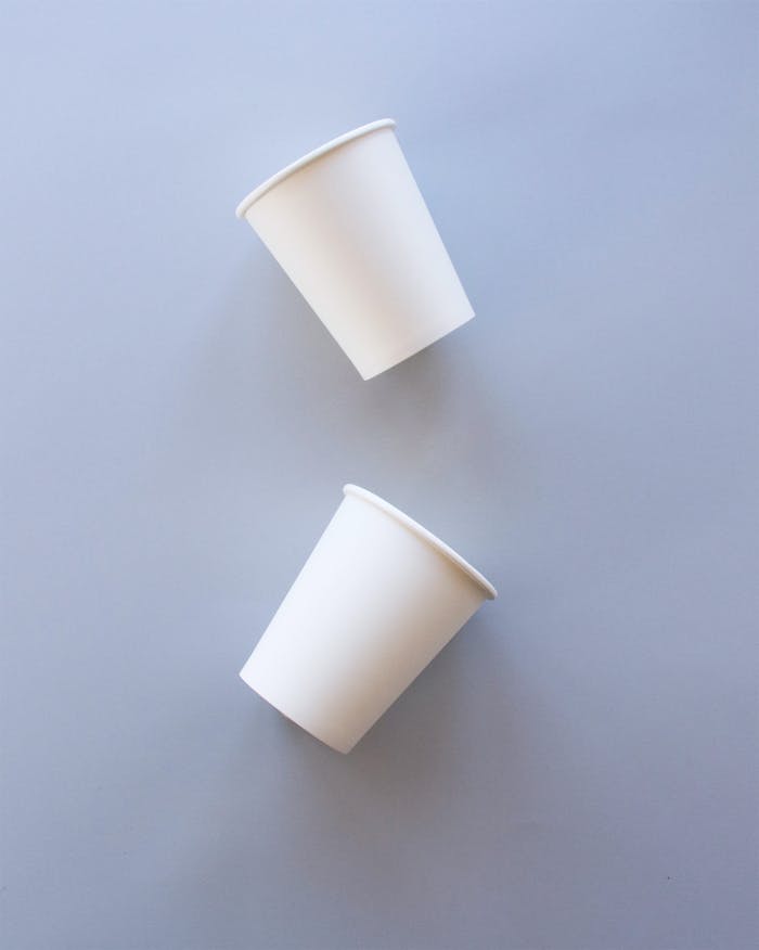 A minimalist flat lay of two white paper cups on a grey background.